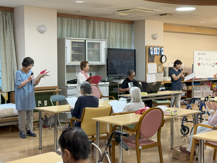 利用者の前で歌う3人と、アコーディオンを弾く高田さんの画像。利用者が拍手をしている。