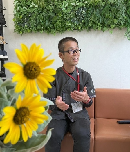 三宅さんがインタビューを受けている様子を写したもの。卓上のひまわりが写っている。