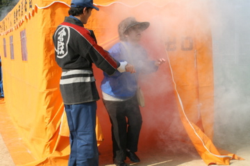 住民が煙体験を行っている　消防団員が指導している写真